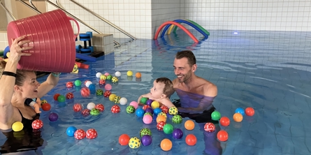 Dame hælder farverige bolde i bassin, far og søn kigger